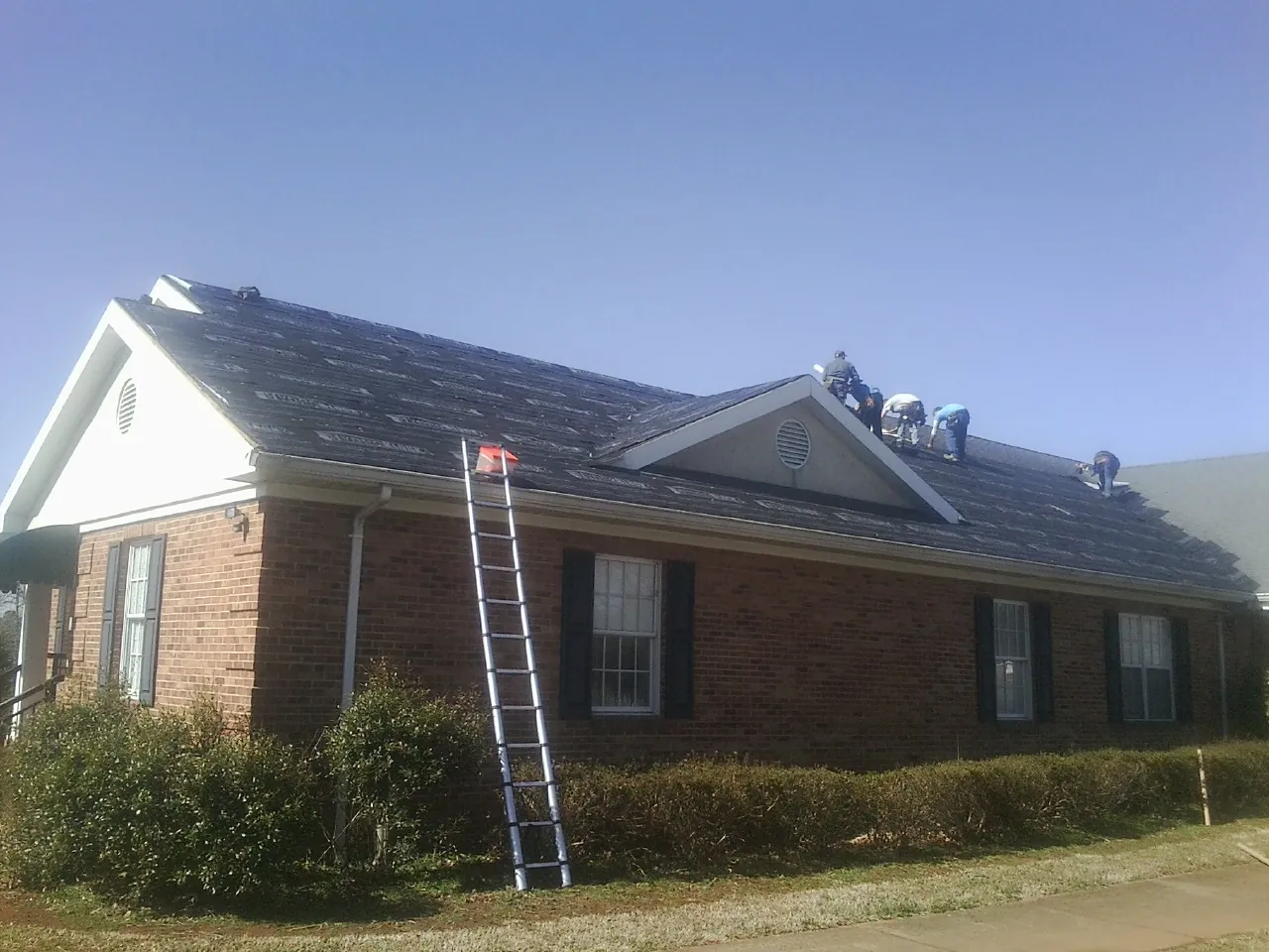 Crew tearing shingles off a brick ranch roof with a ladder set — Emergency Roof Repair work by our crew in Hood River