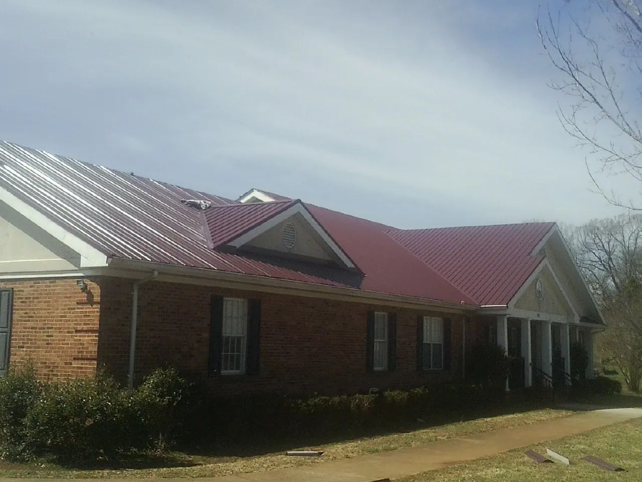Red metal roof with gabled entries on a long brick building, from a Hail Damage Roof Repair job in Hood River