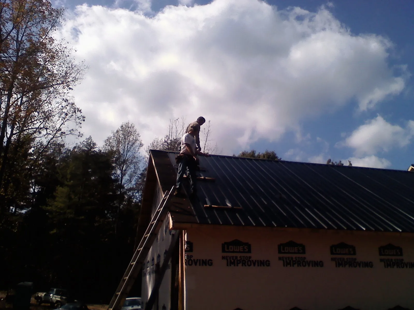 Roofer fastening dark metal panels high against a cloudy sky, from a Roof Inspection job in Hood River