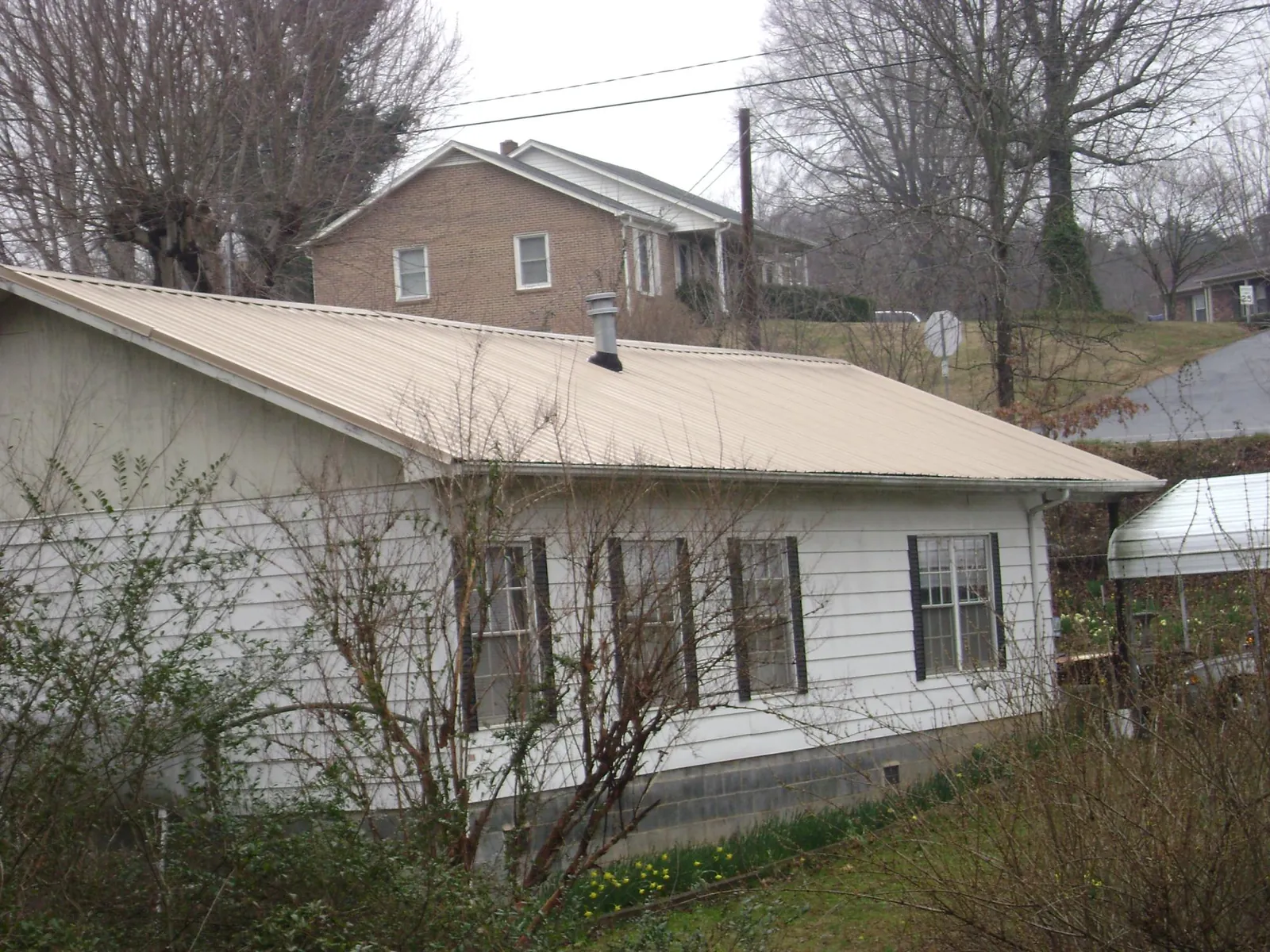Tan metal roof on a white sided house set into a hillside — Commercial Roofing by Roofing Brothers in Hood River